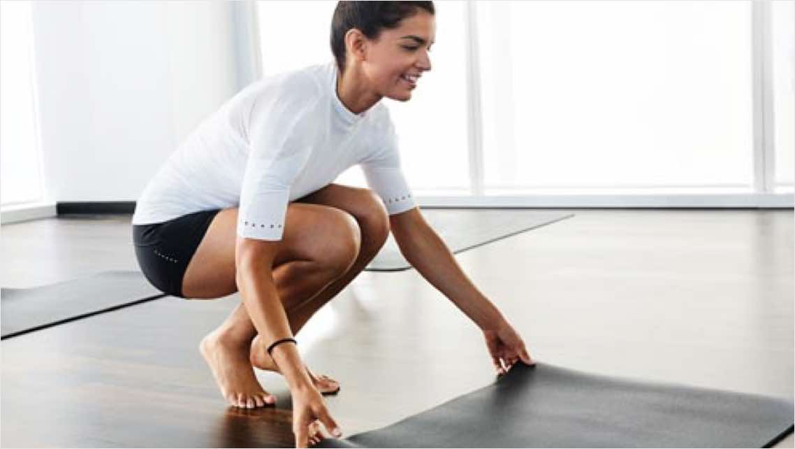 Woman setting out a yoga mat in a group fitness studio at Life Time