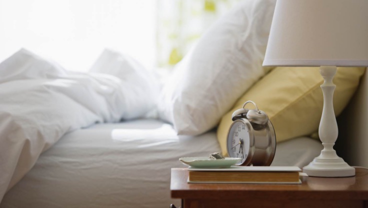 Nightstand with lamp and alarm clock next to a bed