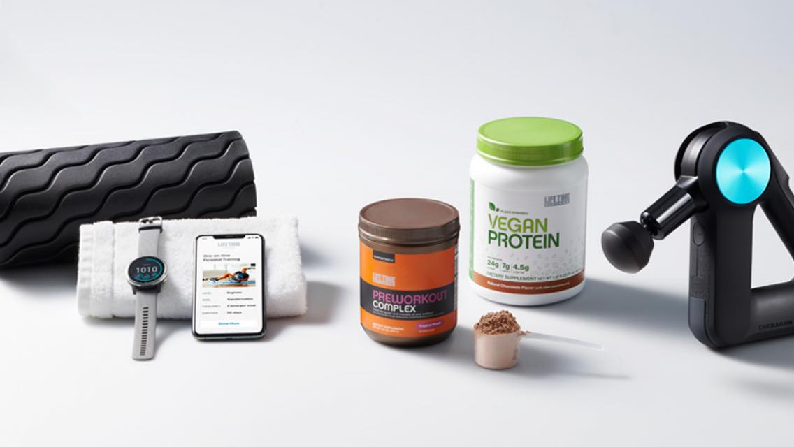 Image of a Theragun, Life Time protein powder, a cell phone showing a training workout, a smart watch and a foam roller.