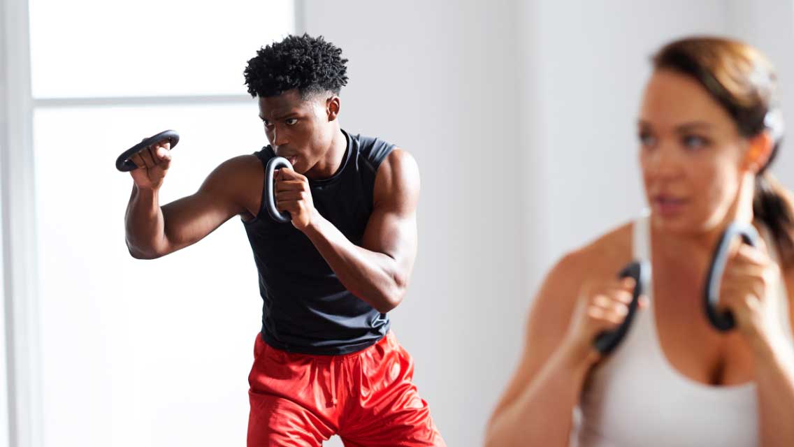 A man and a woman with light weights in their hands punching in a group fitness class.