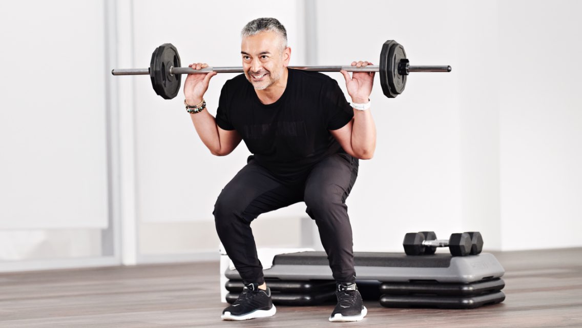 a smiling man completes a barbell squat with barbell on his shoulders