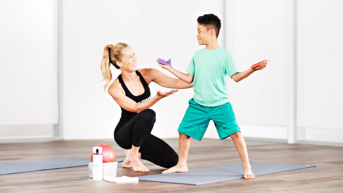 a woman instructor instructs a young boy performing a barre pose