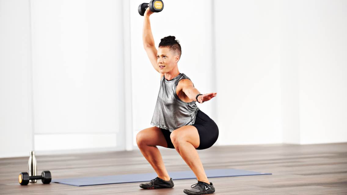 a woman performs a squat with overhead dumbbell press