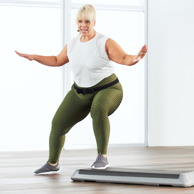 Woman taking a step and strength class at home with Life Time Classes On Demand