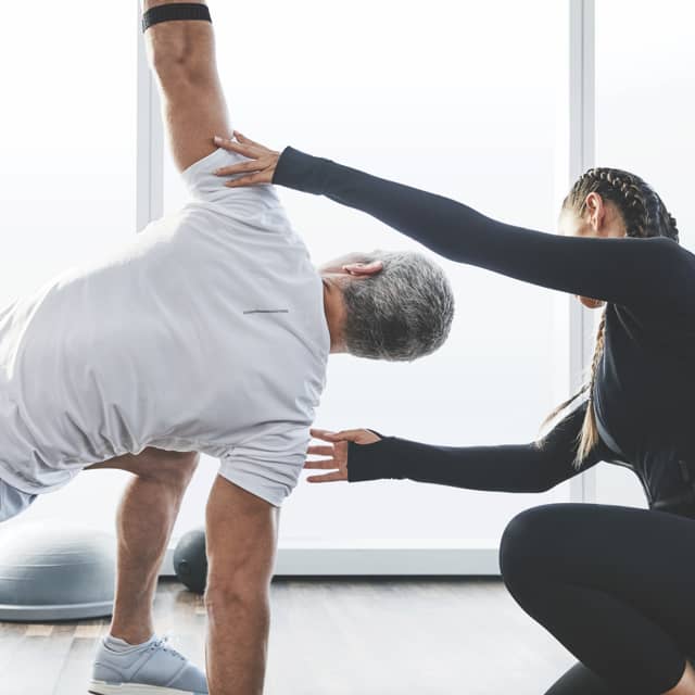 A Life Time trainer helps her client complete a side stretch 