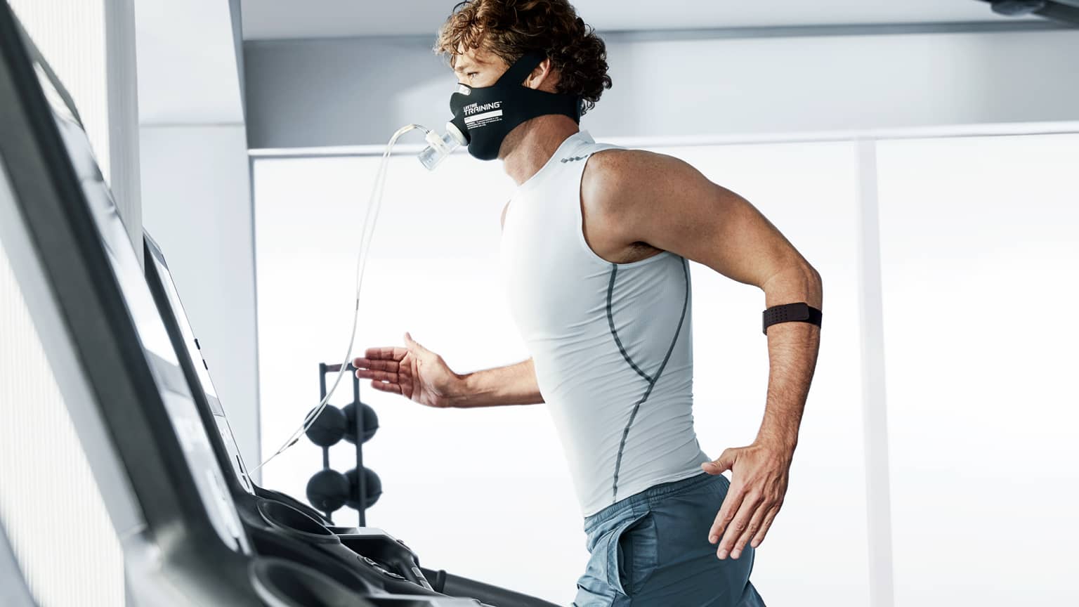 A Life Time member wearing a face mask and heart rate monitor runs on a treadmill