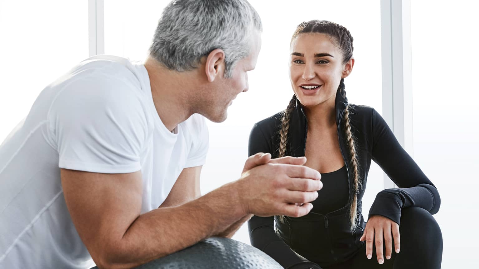 A smiling trainer and her client speak together in a sun-filled room