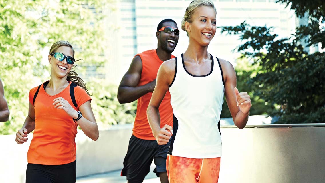 A group of four people in a run club running around a corner with green, leafy trees in the background