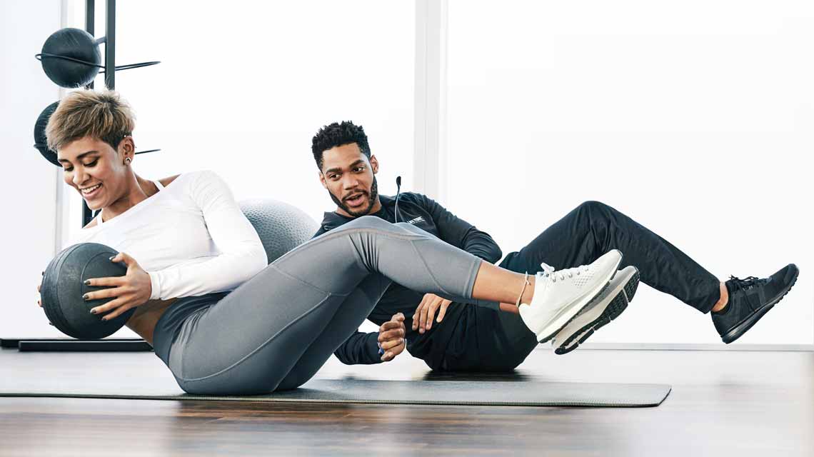 A Personal Trainer and his client sitting on the fitness floor completing abdominal exercises with a medicine ball