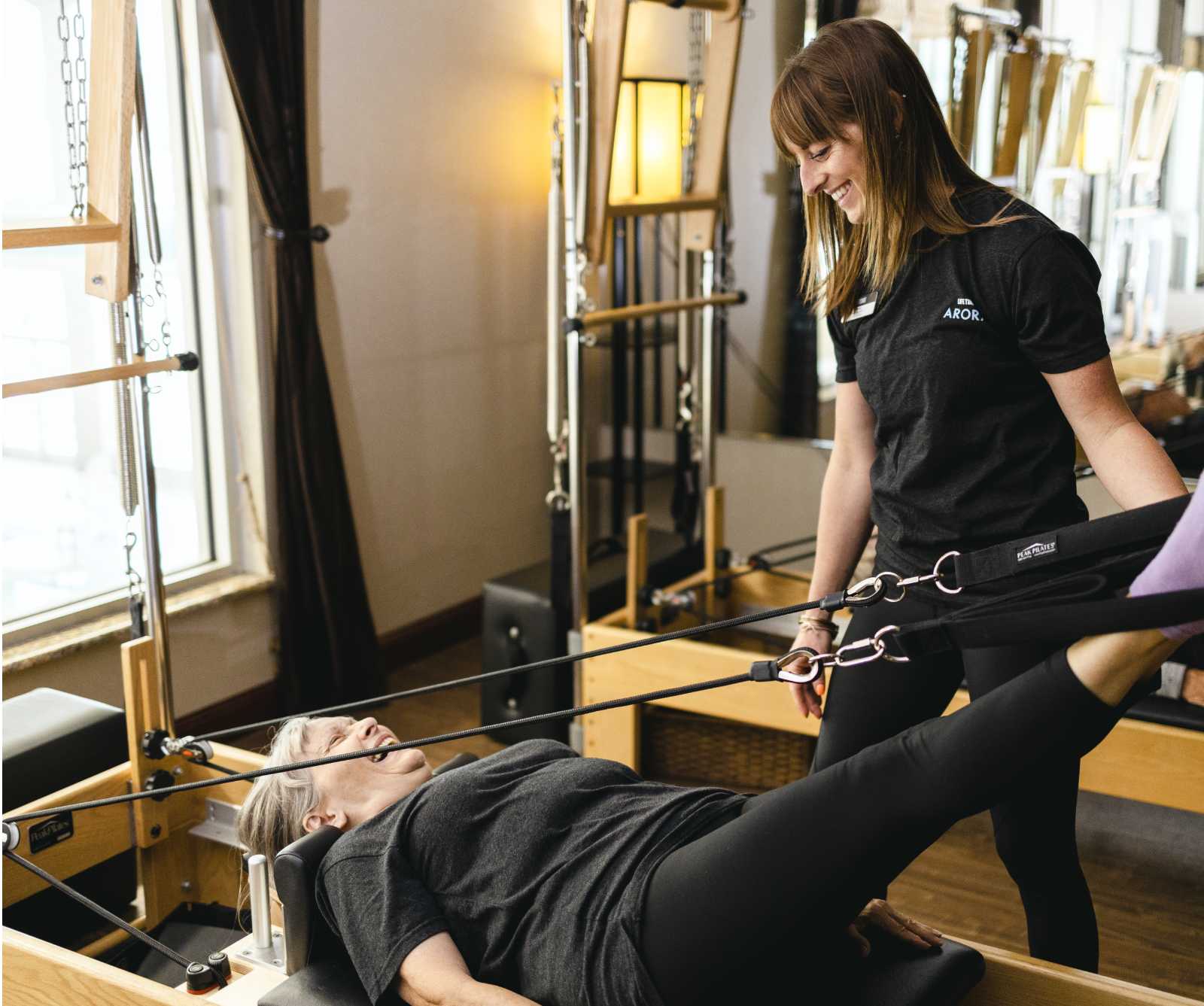 A pilates instructor helps a woman perform a movement on the pilates reformer machine