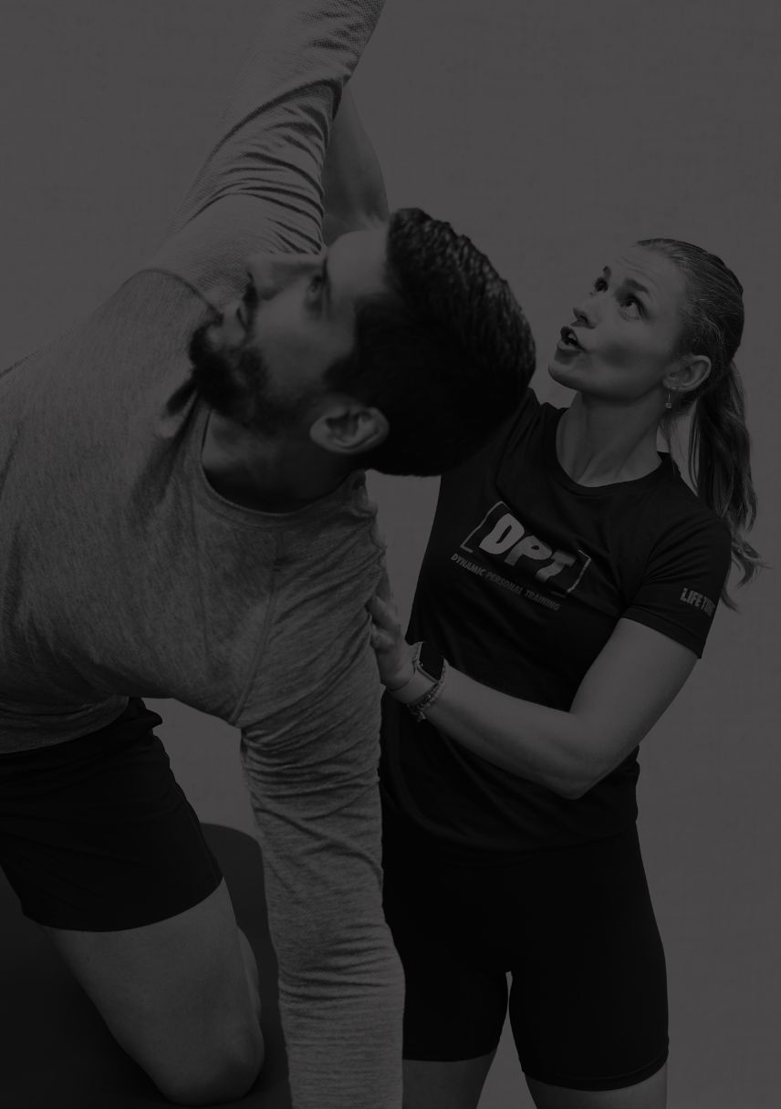 A female trainer stands behind her male client providing manual assistance to help him move deeper into a stretch.